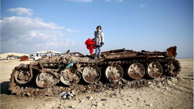 Girl stands on remains of destroyed tank in Yazi Bagh, north-west Syria (Feb2019)