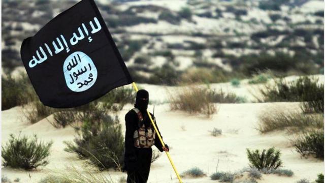 مقاتل من تنظيم الدولة يرفع راية التنظيم في مكان ما من الصحراء في العراق أو سوريا