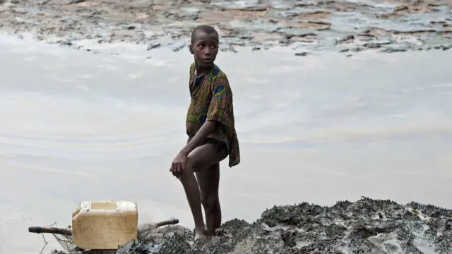 A boy with a fishnet standing on the oil stained bank of a creek near Goi, Ogoniland, Nigeria