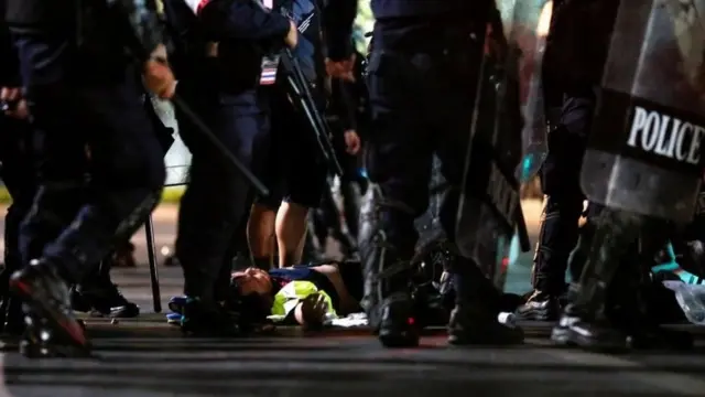 ชายสวมเสื้อกั๊กของอาสาสมัครทีมแพทย์นอนอยู่ท่ามกลางตำรวจหลังถูกคุมตัว