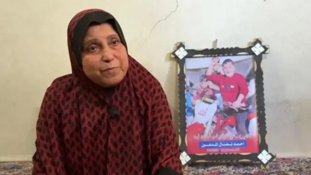 A mãe de Ahmed al Madhoun, com um manto vermelho sobre a cabeça e uma foto de seu filho, na sala de casa.