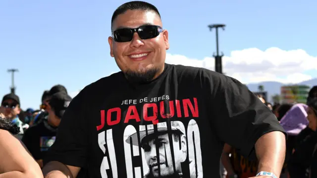 Joven sonriente con gafas de sol que viste una camiseta con la imagen del Chapo