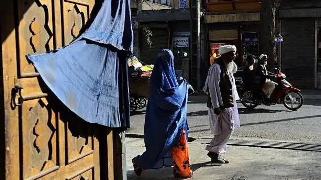 تصویر یک زن که با چادری که در کنار مردی در شهر هرات قدم می‌زند. 