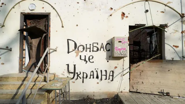 На світлій стіні, пошкодженій пострілами й влучанням фрагментів снарядів, міститься напис "Донбас - це Україна". По обидва боки від нього - увігнуті й іржаві двері. Ті, що ліворуч, - виходять на сходи.