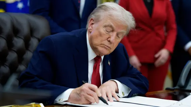 Donald Trump firma un documento en el Despacho Oval.