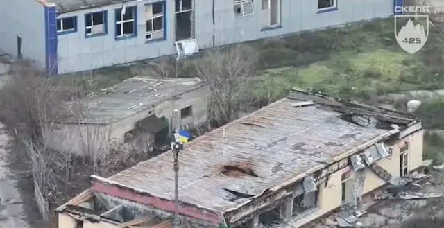 Українські військові встановлюють прапор України на пошкодженій вибухами будівлі.