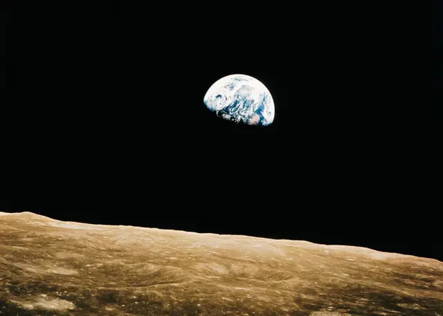 Foto tomada desde la órbita lunar en la que aparece la Tierra parcialmente en la sombra y la superficie lunar en un primer plano.