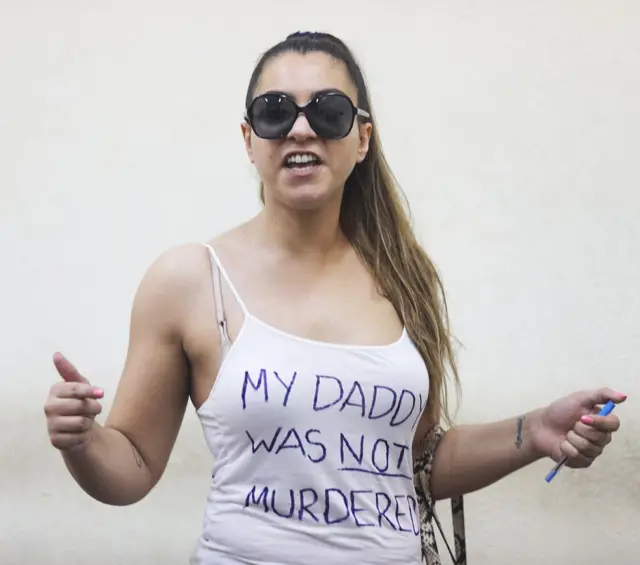 Hellen Veevers wearing dark glasses and a vest top with the words "my Daddy was not murdered" written in pen on it.