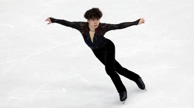 黒い衣装の佐藤が両手を広げながら滑っている