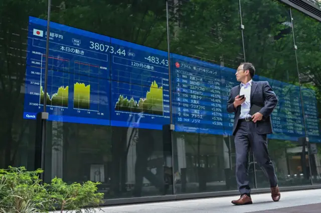 Un hombre camina junto a un panel con información bursátil en Tokio. 