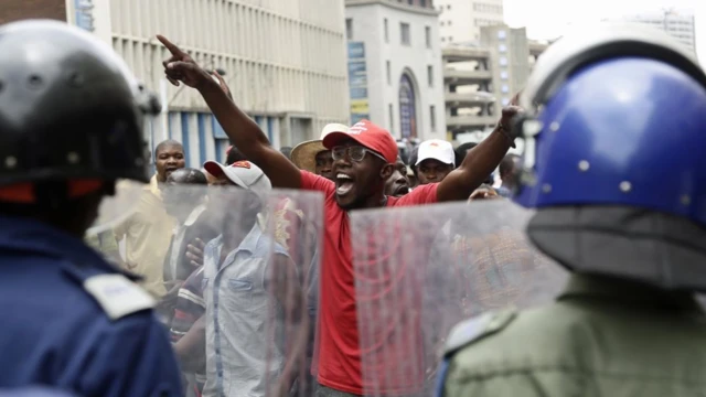 Abigarambya bo mu ishyaka rya Movement For Democratic Change (MDC) muri Zimbabwe imbere y'icyicaro cy'ishyaka ryabo i Harare, polisi icungiye hafi