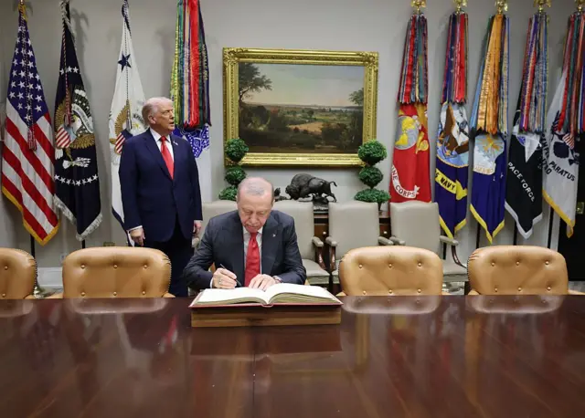 Cumhurbaşkanı Erdoğan Beyaz Saray ziyaret defterini imzalıyor, arkada Trump bekliyor.