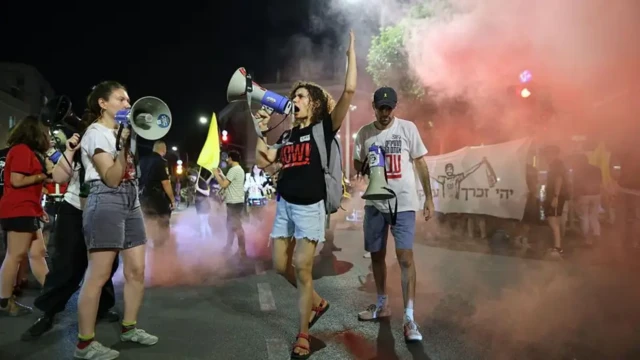 معترضان در خیابانی که دود آن را فراگرفته، سه معترض بلندگوی دستی در دست دارند