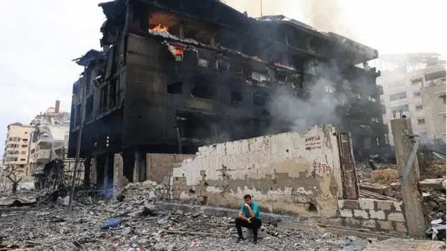 Um homem palestino sentadocasa de apostas betfairfrente a um prédio destruído enquanto um incêndio assola seu interior, após ataques aéreos israelenses no distritocasa de apostas betfairRimal, na cidadecasa de apostas betfairGaza,casa de apostas betfair10casa de apostas betfairoutubrocasa de apostas betfair2023