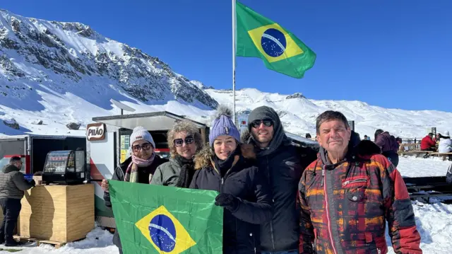 Grupobet ganhacinco pessoas posa para foto segurando bandeira do Brasil; atrás, se vê neve e outra bandeira do Brasil hasteada