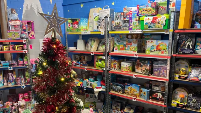Se muestra una habitación con un árbol de Navidad y estantes con juguetes.