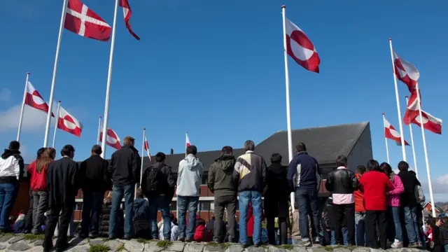 أشخاص يقفون أمام علمي الدنمارك وغرينلاند