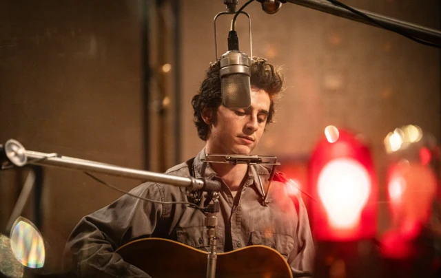 Timothée Chalamet mikrofonun önünde, gitar çalıyor