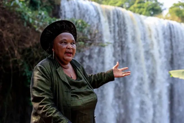 A woman gestures towards a powerful waterfall.