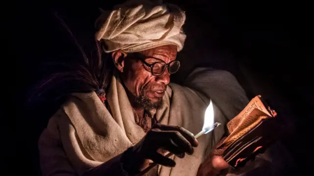 A pilgrim praying with candle lit at night outside the Biete Medhane Alem