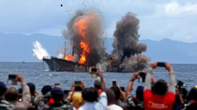People take pictures of a burning ship as the government destroyed foreign boats at Morela village in Ambon island
