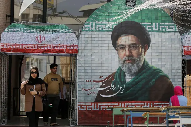 İran'ın yeni ruhani lideri Mücteba Hamaney duvara yapılmış resminin yanında bir kadın ve bir erkek yürüyor.