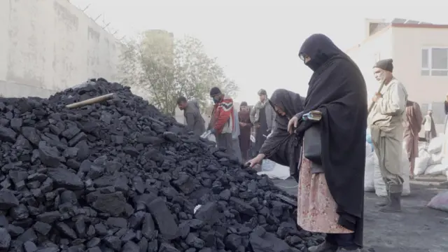 زنی در کنار خروار از زغال سنگ در یکی از مراکز توزیع در شهر کابل نوامبر ۲۰۲۵
