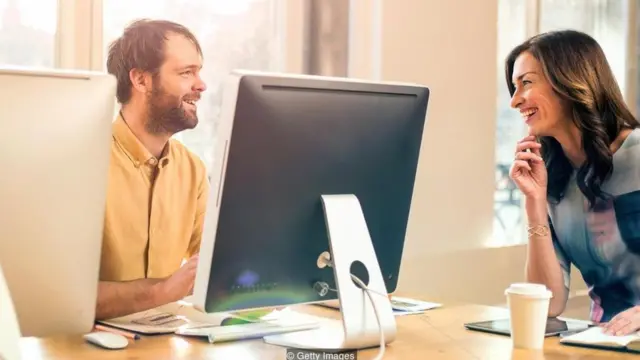 Hombre y mujer sentados en una oficina, que conversan y sonríen
