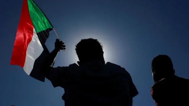 A protestor holding up a Sudan flag against a dark blue sky in Khartoum Sunday 21 November 2021