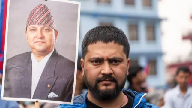 त्रिभुवन आंतरराष्ट्रीय विमानतळावर एका समर्थकाने माजी राजा ज्ञानेंद्र शाह यांचा फोटो धरला आहे