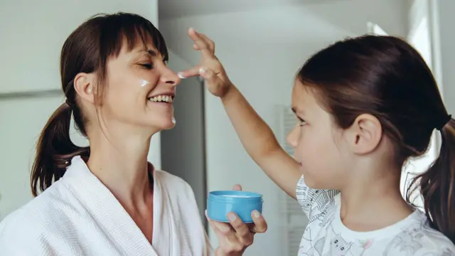 Filha passando creme facial no rosto da mãe.
