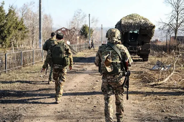 Soldados de costas e tanque em estrada de terra