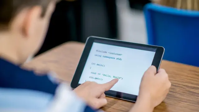 Menino olha para uma linguagem de programação em um tablet