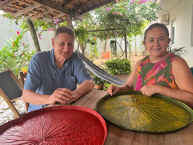 Casal sorrindofrente a mesa, sobre a qual estão jogos americanos