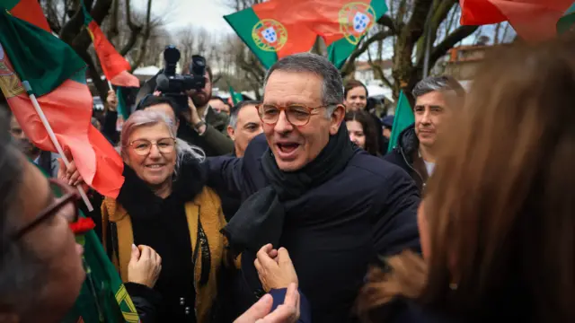 Homem de óculos no meio de várias pessoas com bandeiras de Portugal