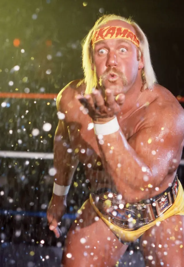 Hulk in the ring with his trademark yellow bandana and trunks and a gold belt, blowing sparkling dust or confetti out of the palm of his hand in 1987