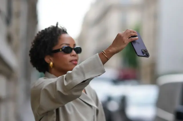 Una mujer sujeta un iPhone con dos dedos. 