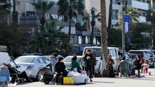 Saldırıdan kaçan insanlar kaldırımda oturuyor yanlarında araçlar park etmiş.