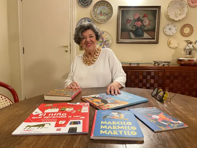 Ruth sorrindo sentada diante de mesa com vários livros