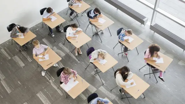 Foto tirada do alto mostra várias crianças fazendo atividade com papelgoiás e atlético paranaense palpitesuas carteiras da escola