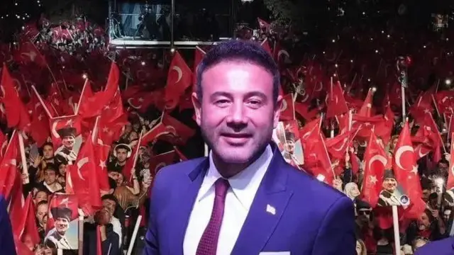 Eski Beşiktaş belediye başkanı Rıza Akpolat bir kutlama etkinliğinde. Arkasında elinde Türk bayrağı bulunan kalabalıklar görünüyor. 