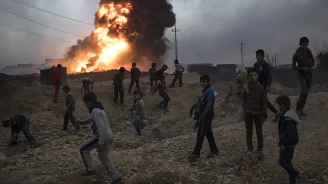 Crianças nos escombros e fogo ao fundo