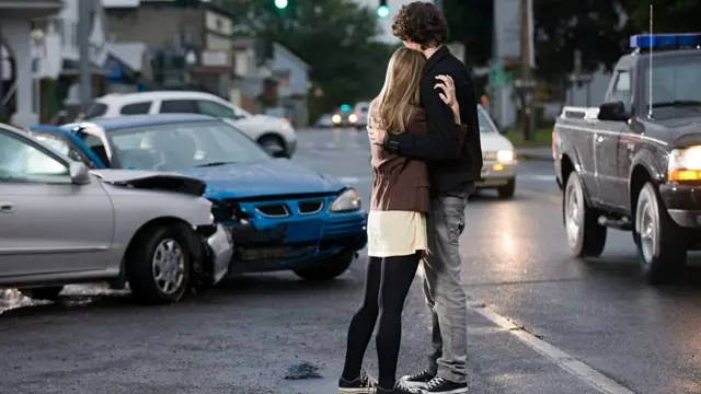 Jovens abraçados enquanto olham carros batidos