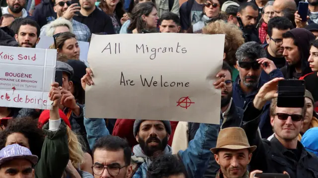 Members oWanachama wa mashirika ya kutetea haki za binadamu wakiwa wamebeba mabango wakati wa maandamano, baada ya Rais wa Tunisia Kais Saied kuamuru vikosi vya usalama kusimamisha uhamiaji haramu na kuwafukuza wahamiaji wote wasio na vibali, huko Tunis.f rights groups carry banners during a protest, after Tunisian President Kais Saied ordered security forces to stop all illegal migration and expel all undocumented migrants, in Tunis.