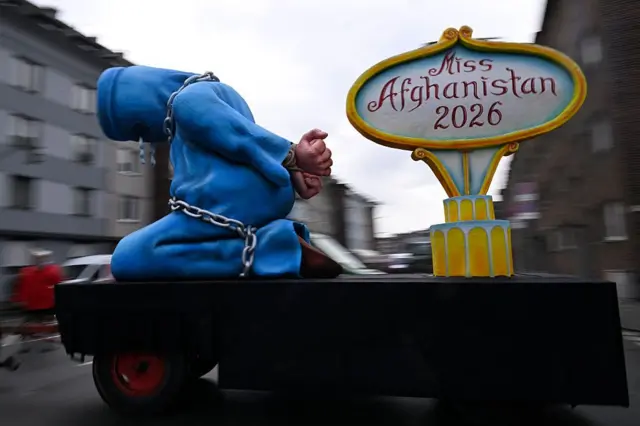 مجسمه آبی زن روی یک سکو در خیابان کشیده میشود. دستش به پشت بسته شده و زنجیر دور بدنش پیچیده شده است.