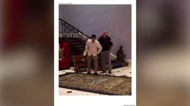 ਐਪਸਟੀਨ ਇੱਕ ਆਦਮੀ ਨਾਲ ਜ਼ਮੀਨ 'ਤੇ ਪਏ ਕੱਪੜੇ ਦੇ ਇੱਕ ਟੁਕੜੇ ਨੂੰ ਦੇਖਦੇ ਹੋਏ