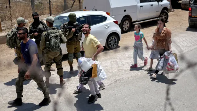 يسير الدروز حاملين أمتعتهم على خط وقف إطلاق النار بين مرتفعات الجولان وسوريا أثناء عودتهم إلى سوريا، بالقرب من قرية مجدل شمس الدرزية في مرتفعات الجولان