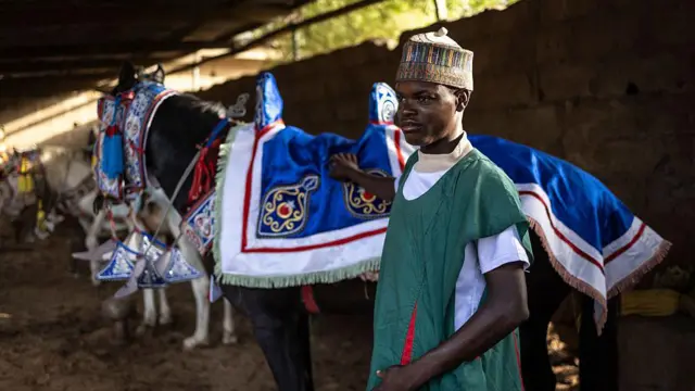 A stable hand strokes a horse which is adorned in a blue satin cloth