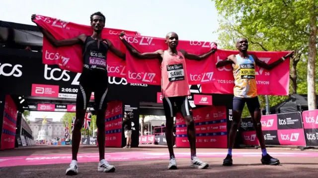 バッキンガム宮殿を遠く背にした大通りパルマルに設けられたゲートの前、上位3人の選手がピンクの大会バナーを両手で自分の後ろに広げて並んでいる。ウェアにそれぞれの名前が書かれたゼッケンをつけている