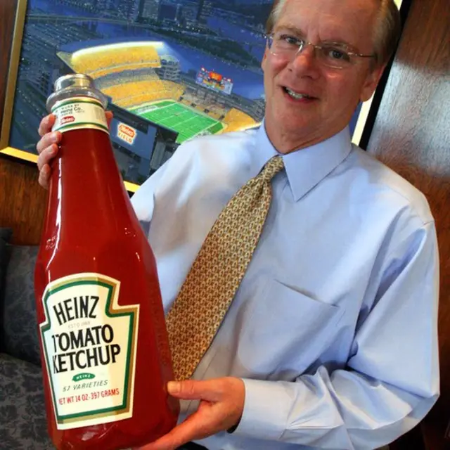 El director de Heinz William R. Johnson sosteniendo una botella enorme de ketchup
